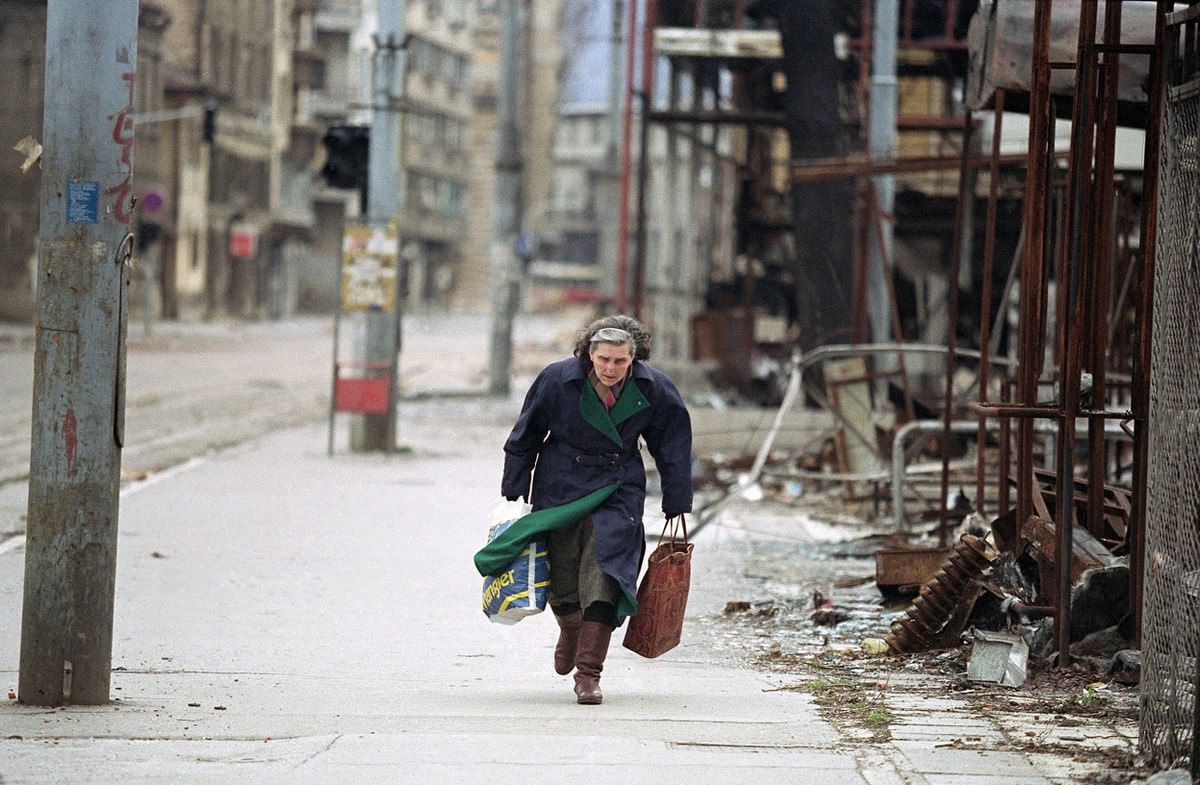 Bosnian woman rushes down an empty sidewalk past war-destroyed shops in one of the worst sections of the so-called "Sniper Alley."