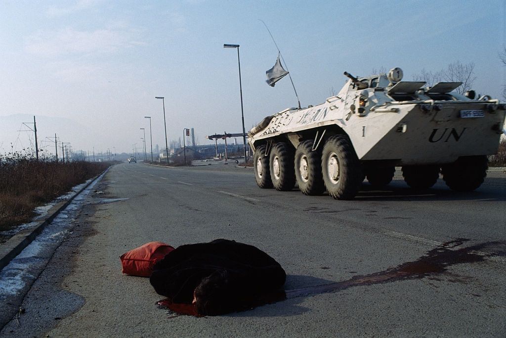 Corpse of a woman lies in the road next to a United Nations medical vehicle.