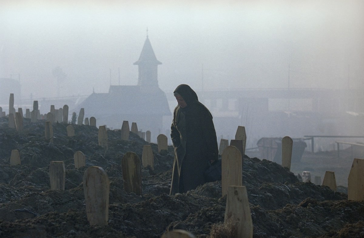 A woman, standing between markers of fresh graves in a Sarajevo cemetery, mourns over the grave of a dead relative in the early morning, on January 17, 1993.