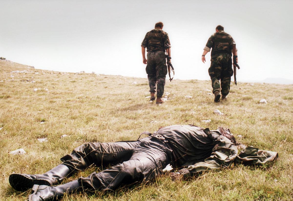 Two Bosnian Croat soldiers pass by the corpse of a Bosnian Serb soldier killed in the Croatian attack on the Serb-held town of Drvar, on August 18, 1995 in western Bosnia.