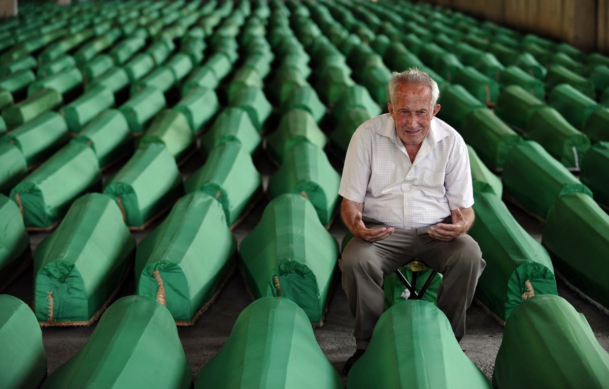 A Bosnian muslim man gestures as he mourns among caskets at Potocari Memorial Cemetery near Srebrenica
