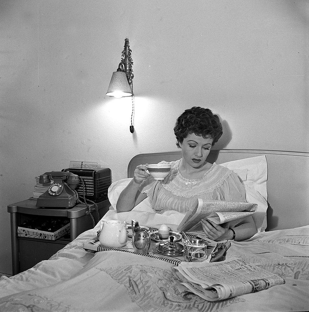 Margaret Lockwood is pictured reading the newspapers as she enjoys breakfast in bed, 1950