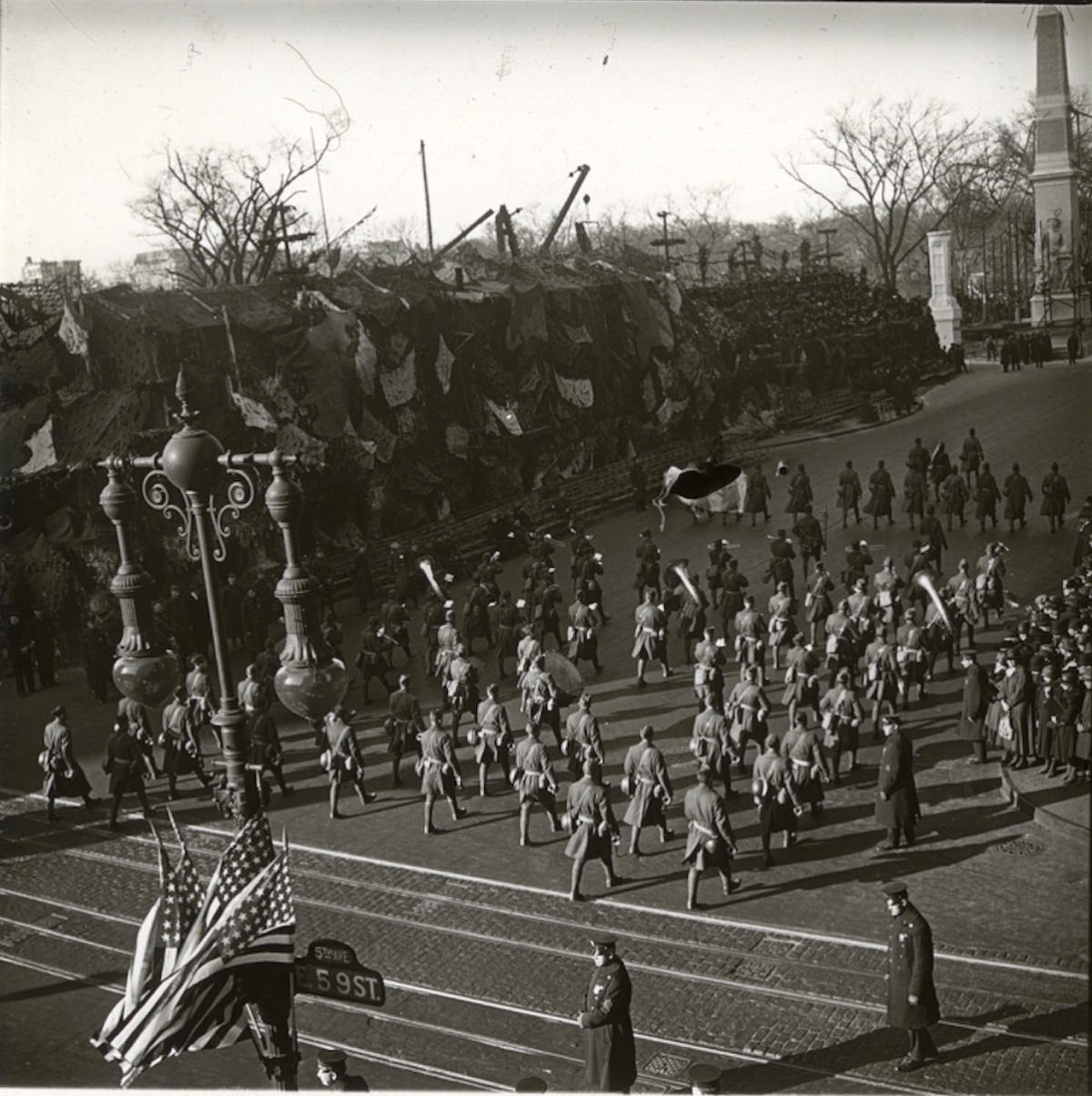 Soldiers on parade, marching north on Fifth Avenue. Note the street sign on the light pole: 59th Street and 5th Avenue. A part of the Arch of Jewels is visible at top right.