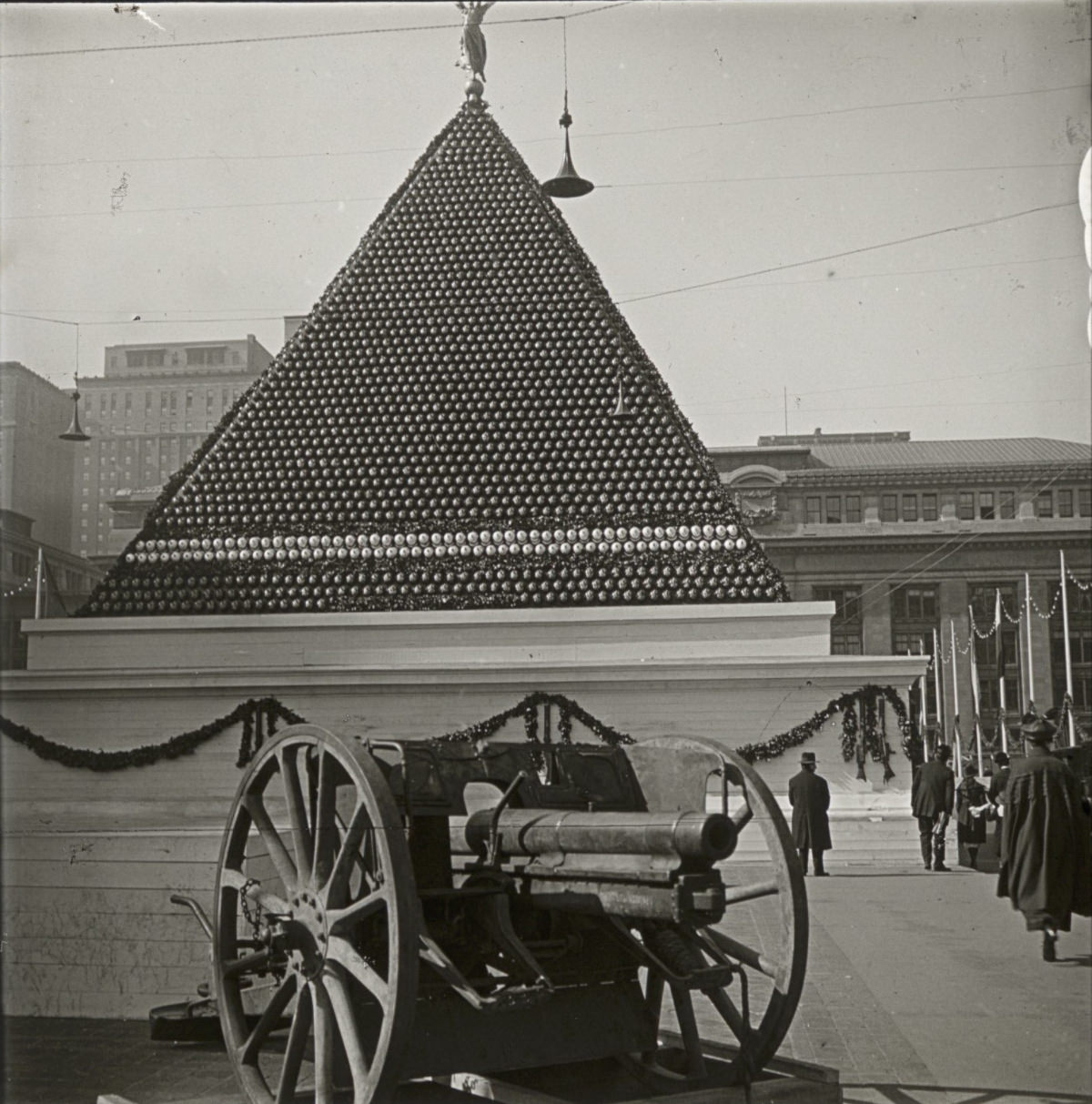 This is quite a visual–a pyramid built of what appears to be artillery shells, with a gun in the foreground.