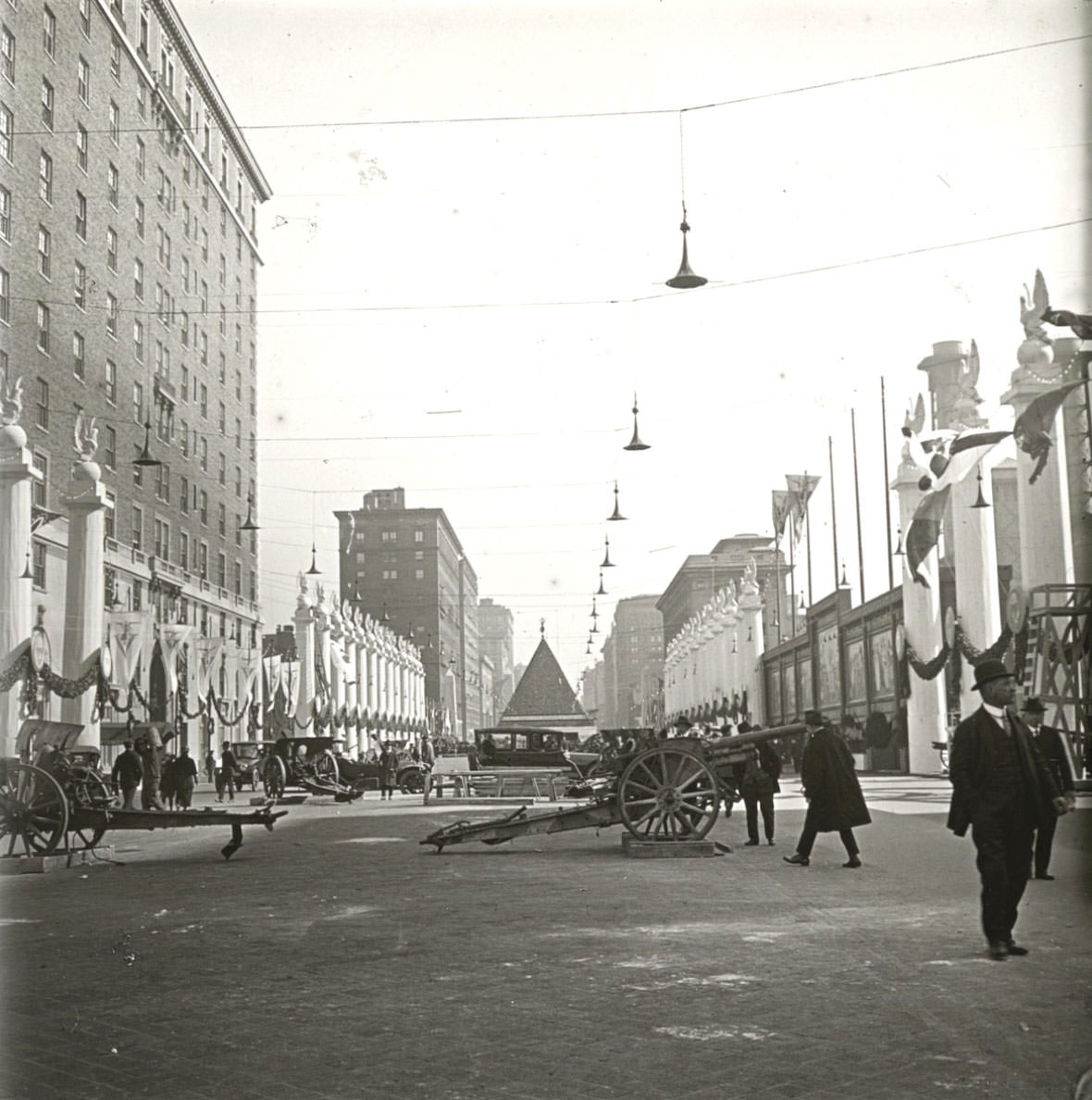 A longer view, on a Manhattan avenue, with artillery guns, columns, and murals in the mid-ground and the pyramid, surrounded by more columns, in the distance.