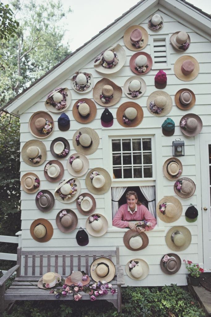 Hat designer Darcy Creech appearing from the window of a house with its facade covered with hats, September 1991