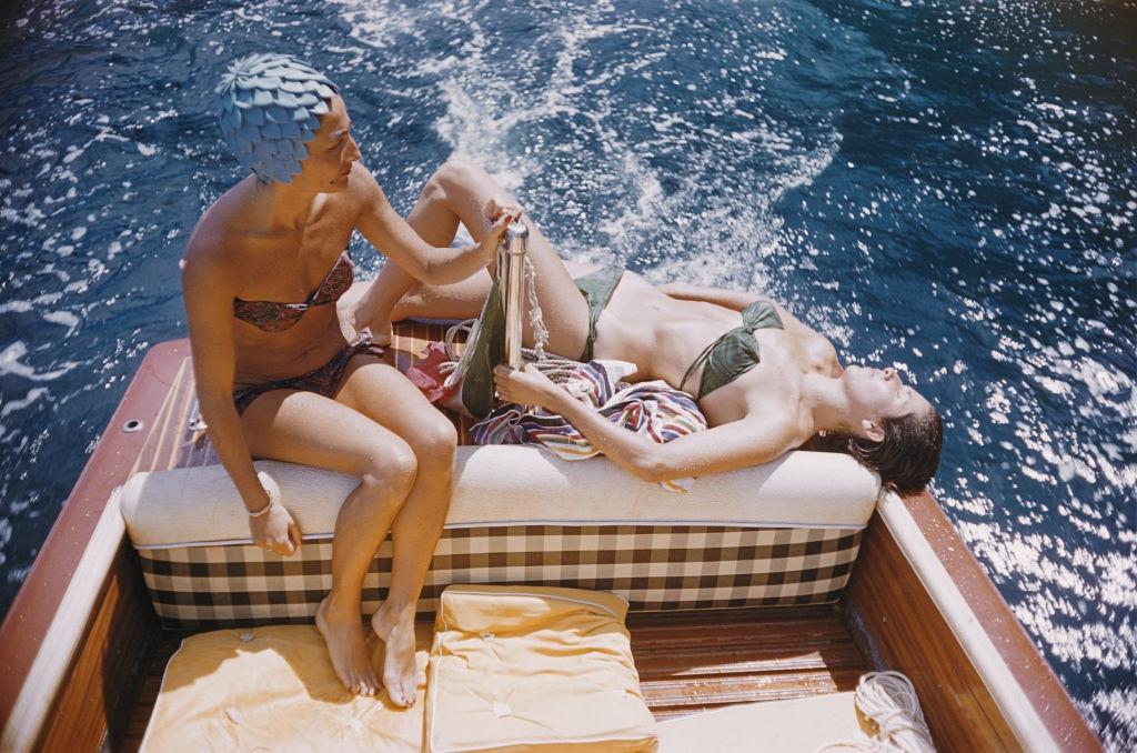 Carla Vuccino, in a swimming cap, and a sunbathing Marina Rava, both wearing bikinis as they sit on the rear of a boat off the coast of the island of Capri, Italy, 1958.