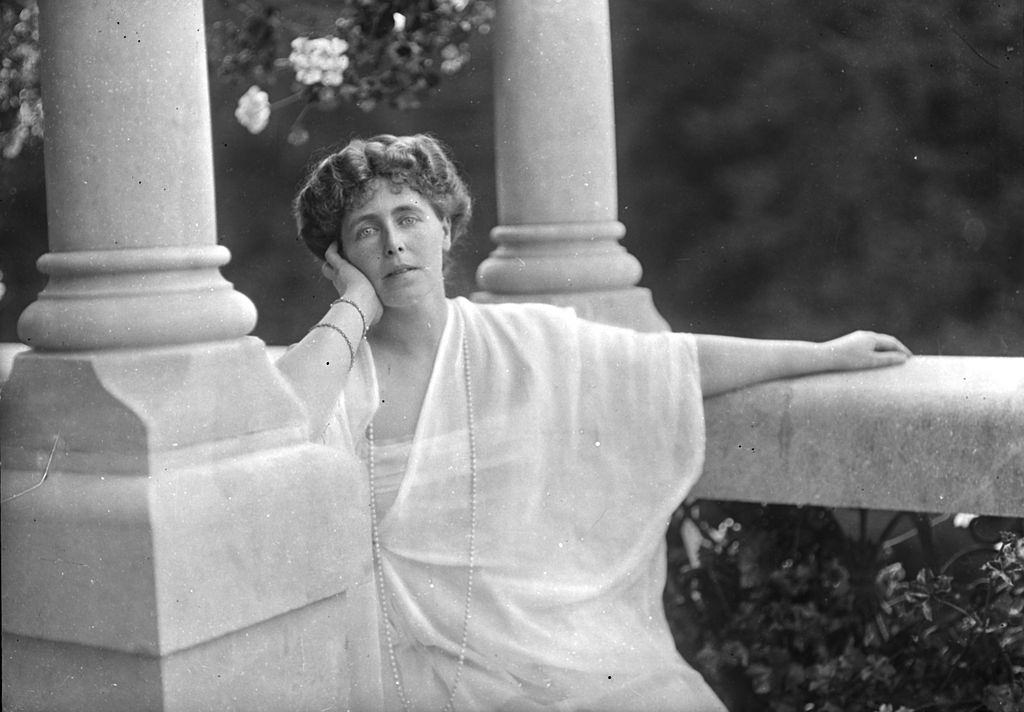 Princess Marie of Romania sits oudoors amid several marble columns, early 20th century.