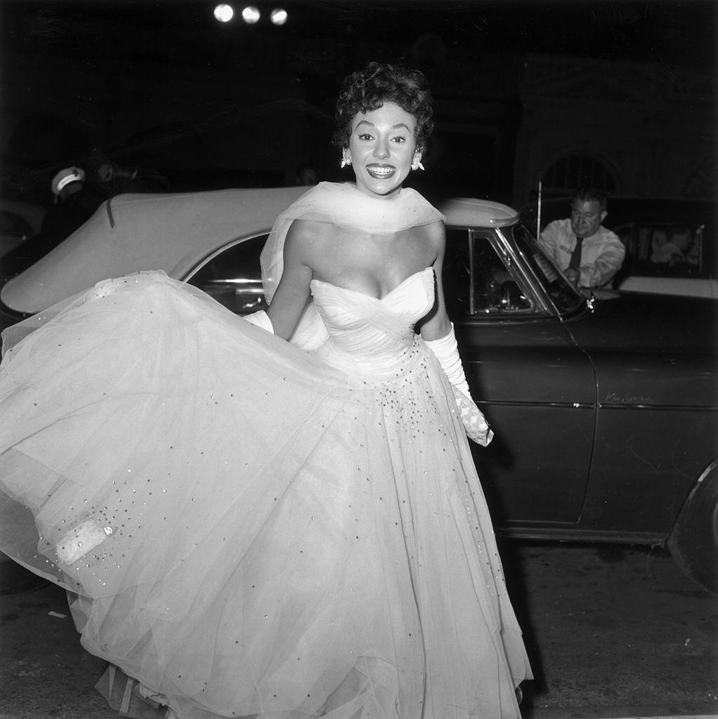 Rita Moreno warnig a white evening gown and arriving at the premiere of director Charles Walters' film 'Lili', 1953.