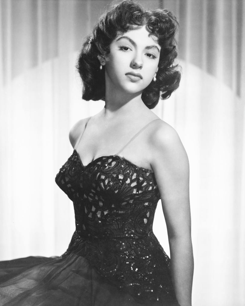 Rita Moreno wearing a black thin strap dress in a studio portrait, 1955.