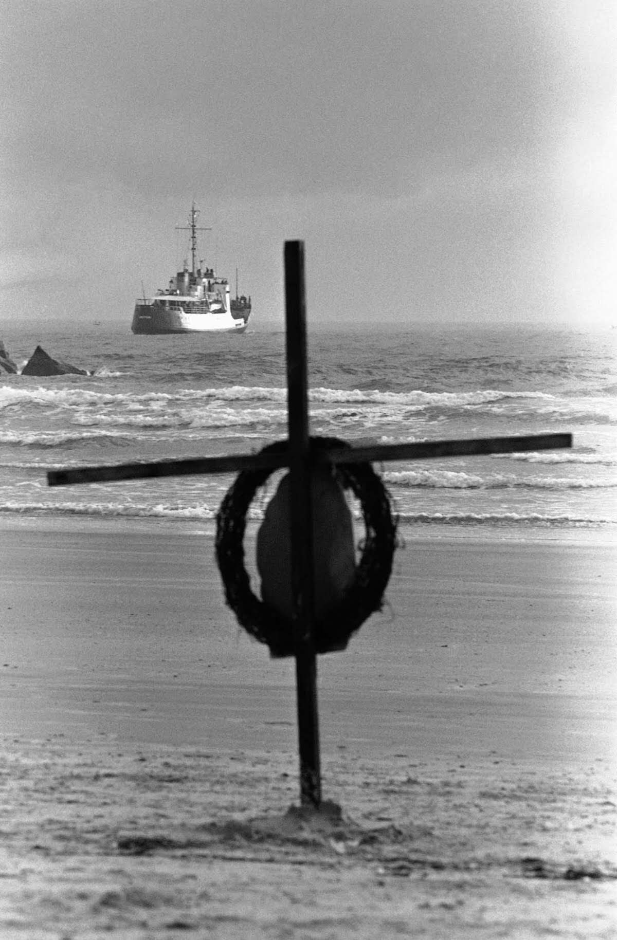 A cross and wreath stand on the beach as a Coast Guard cutter heads out to search for debris from the explosion. February 1986.