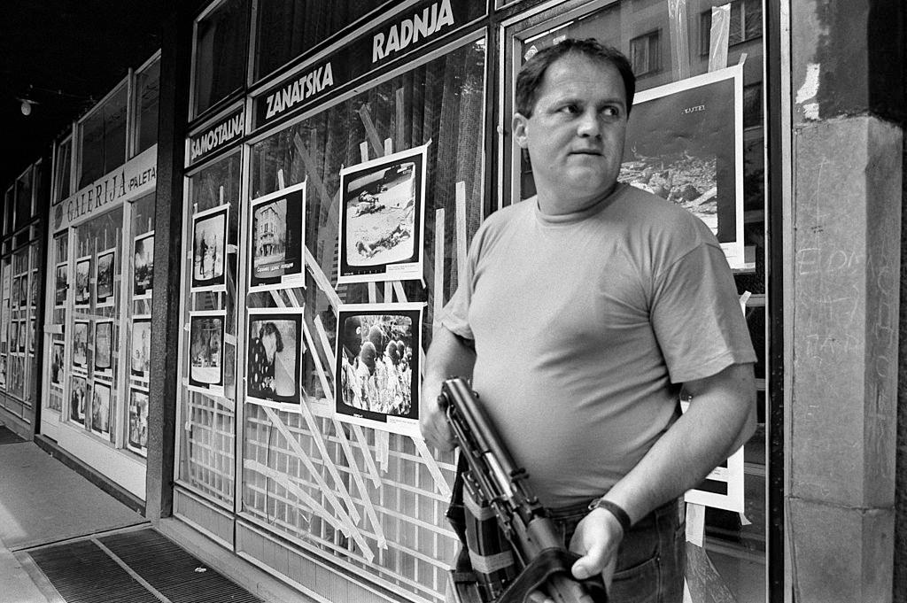 A Bosnian fighter armed with an AK-47 stands in front of images of massacres, alledgedly by Serbian forces.