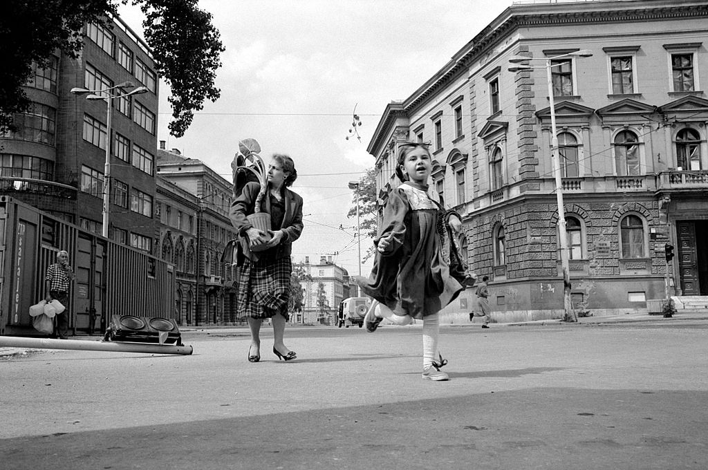 A mother carrying a potted plant runs across Sniper Alley with her young daughter.