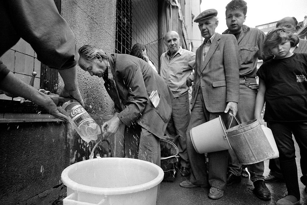 Residents collect water in buckets and coca-cola bottles from a stand-pipe on a Sarajevo street, July 1992.