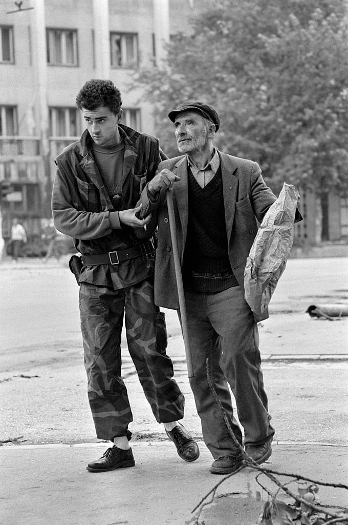 A Bosnian fighter ignores the risk from snipers to bravely help an elderly man cross a dangerous intersection on Sniper Alley, July 1992.