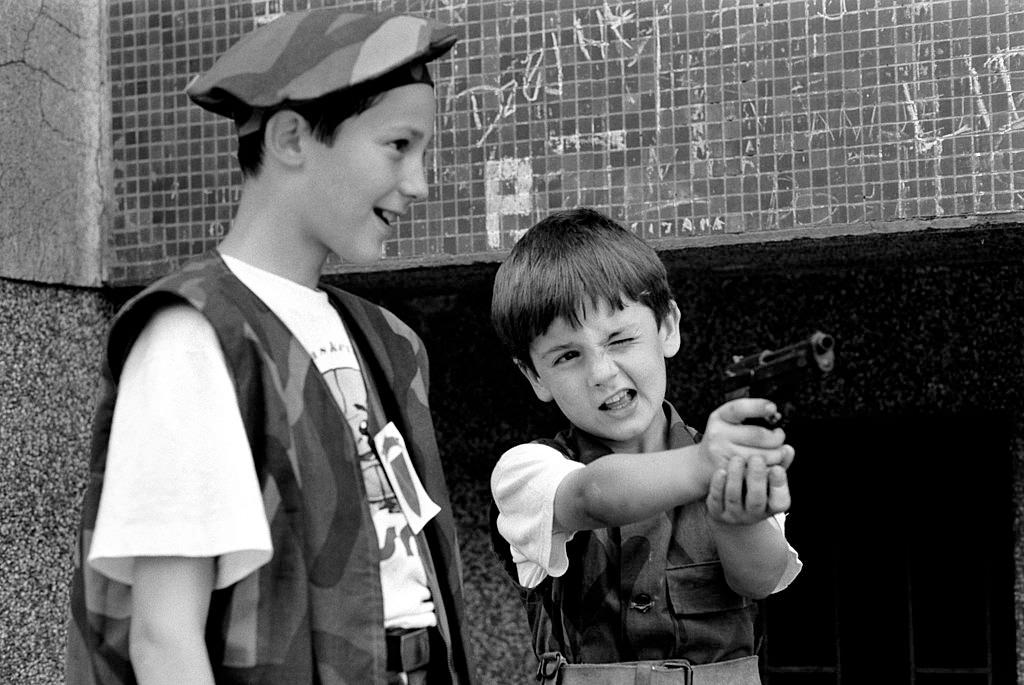 Boys dressed in the uniform of Bosnian army fighters play with a real pistol, July 1992.
