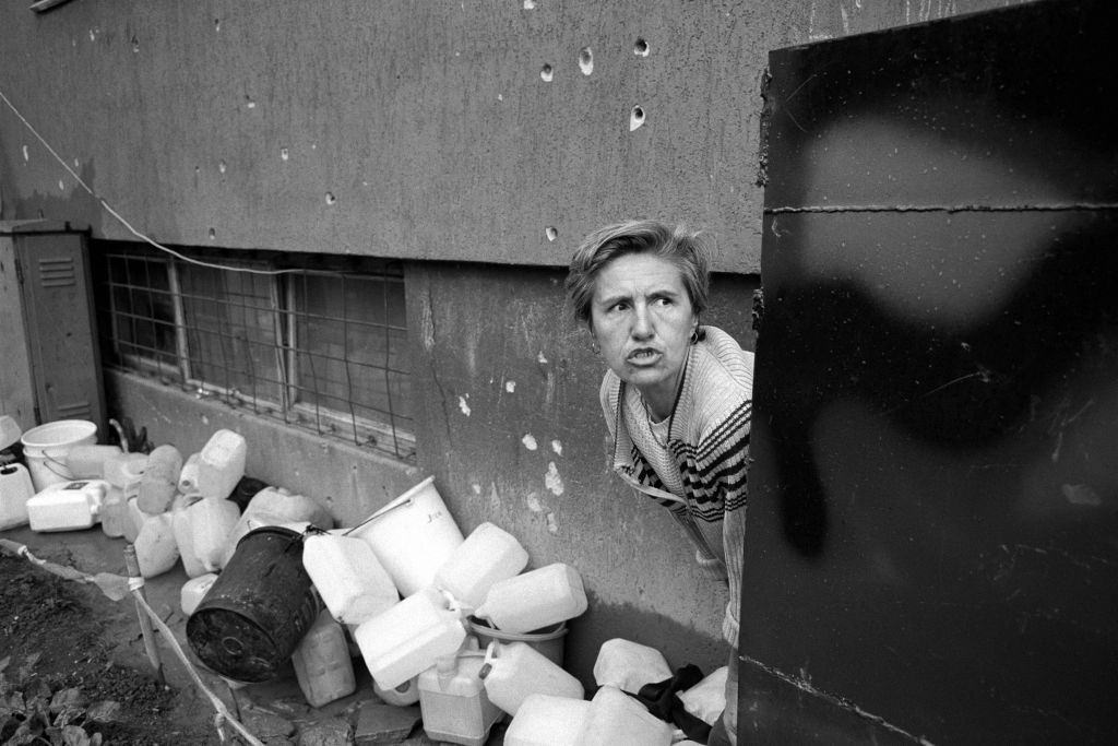 A frightened woman collects water at a stand pipe during an exchange of gunfire between Bosnian and Serbian fighters, July 1992.