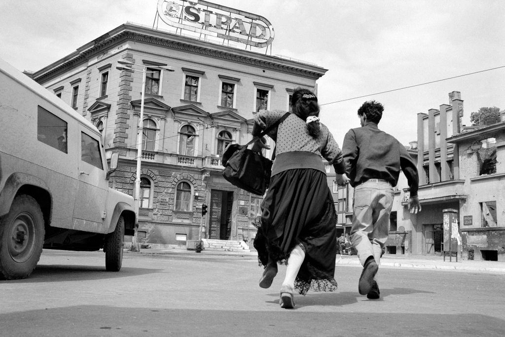 A couple hold hands and shelter behind an armoured press vehicle as they run across an intersection in Sarajevo, 1992.