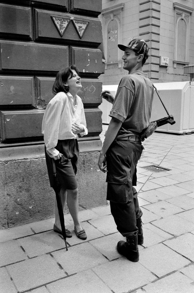 A teenage girl and a young Bosnian fighter with an AK-47 flirt on a street corner during a break in shelling, 1992.