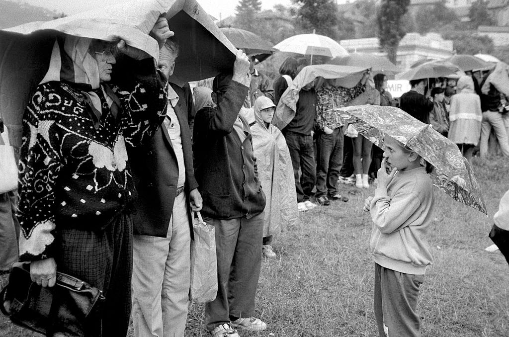 People shelter from the rain under their umbrellas during filming of 'Welcome to Sarajevo' starring Woody Harrelson, 1994.
