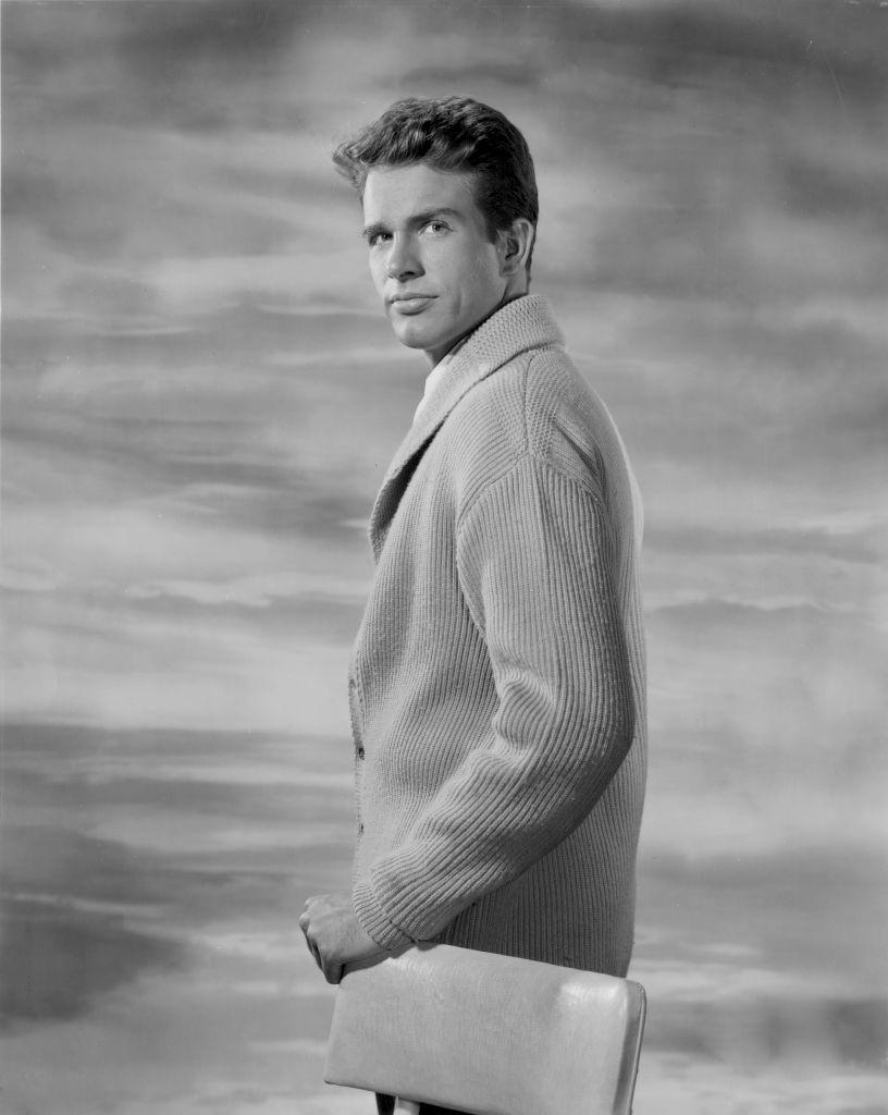 Warren Beatty in a photo studio, with a hand on a chair's back, 1950s.