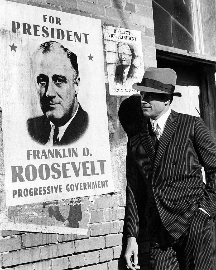 Warren Beatty, as Clyde Barrow, posing next to a Roosevelt campaign poster in a promotional portrait for 'Bonnie And Clyde', 1967.