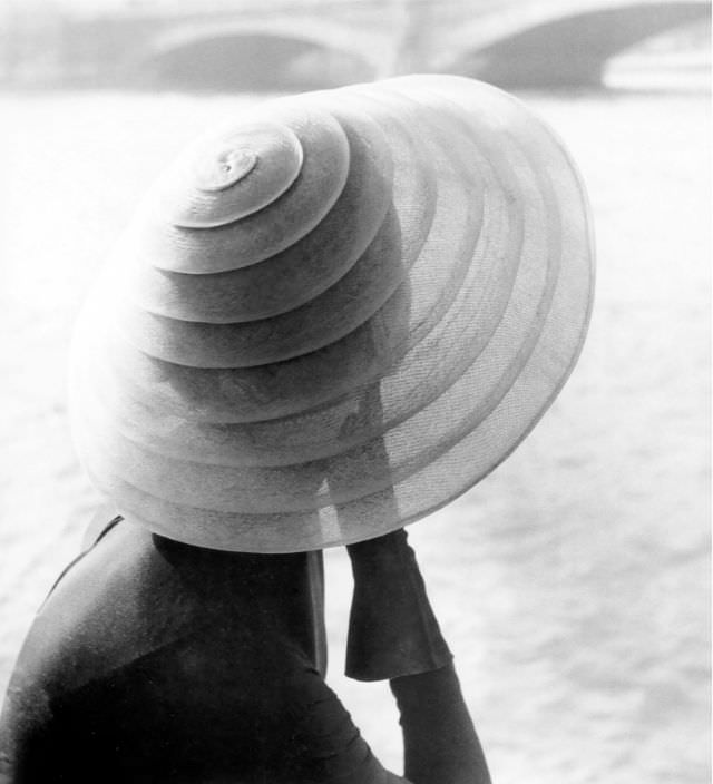 Model wearing hat by Jacques Fath sitting by the river Seine, photo by Regina Relang, Paris, 1951