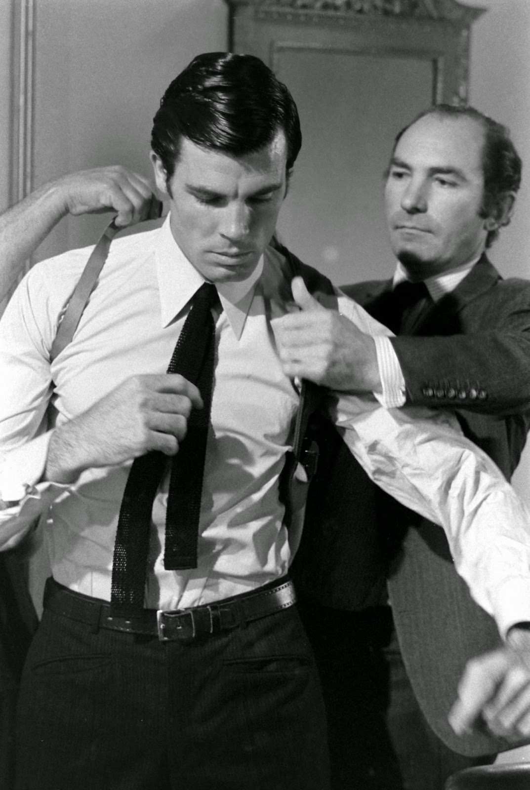 Director Peter R. Hunt helps Robert Campbell get into a shoulder holster, 1967.