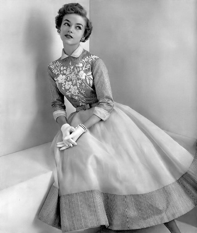 Joan Olson in a blue-striped white organdy dress, the bodice is embroidered in natural strass and beads, by Pierre Balmain, 1954