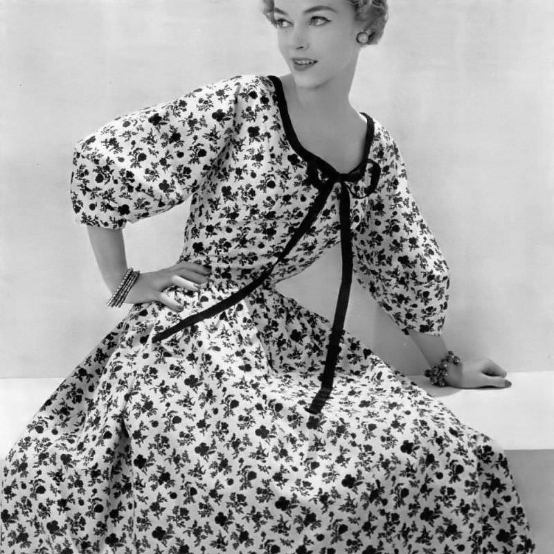 Joan Olson in a romantic cream and black floral print dress bordered in black gros-grain ribbon by Mad Carpentier, 1954