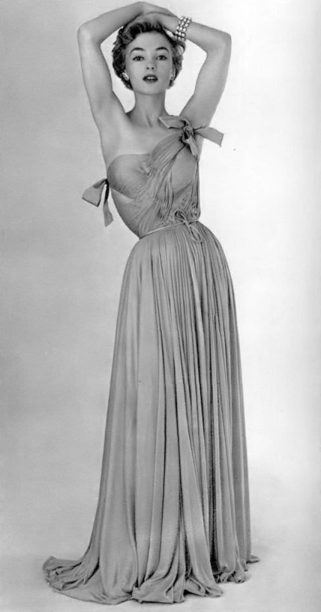 The draped bodice sculpts this jersey gown with pale pink silk, skirt falls loosely, two satin bows adorn the bodice worn by model Joan Olson, by Grès, 1954