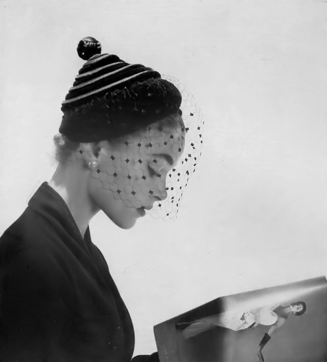 Joan Olson in black velvet and satin spiral that wraps to a point on this small hat with voilette by Le Monnier, 1952