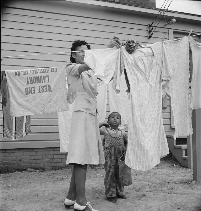A woman hanging out washing with her young son in front of the community building in a FSA (Farm Security Administration) housing relief camp for African Americans, Arlington, Virginia, 1942
