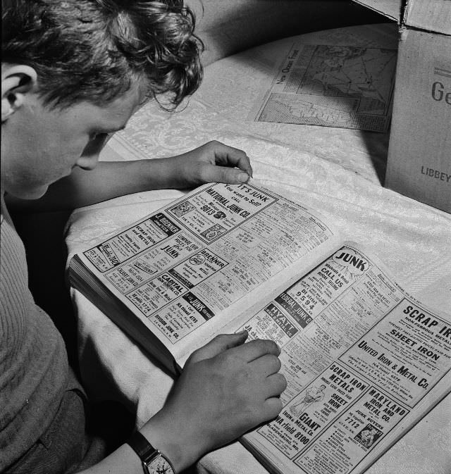 Boy is looking up junk dealers in the telephone directory, wants junk dealer pick up the scrap which he collected stored in his cellar, Washington, D.C., May 1942