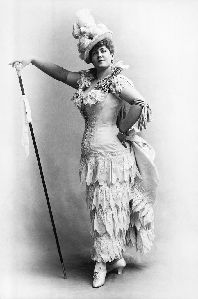 Lillian Russell in one of her typical poses. She is shown full-length, wearing a flounced white dress and plumed hat, 1890.