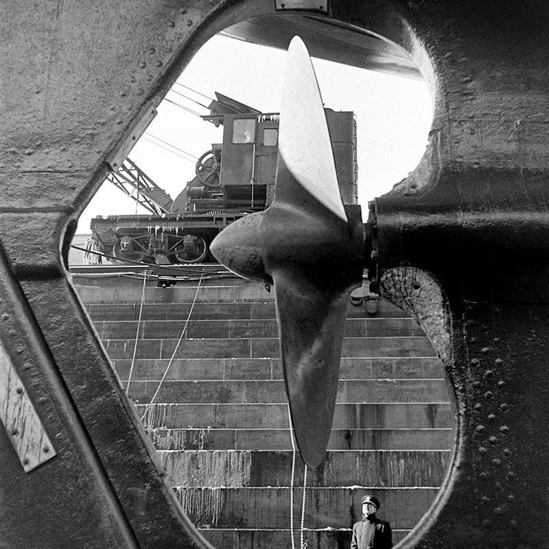 A Naval officer — dwarfed by the vessel in his view — gazes at a cruiser's propeller at the Brooklyn Navy Yard, 1941.