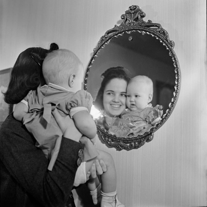 A woman holding an unidentified infant girl in front of a mirror