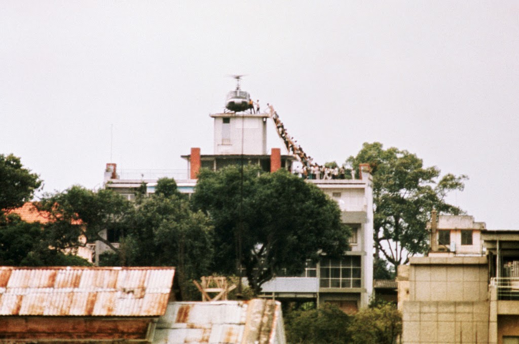 A CIA employee (probably O.B. Harnage) helps Vietnamese evacuees onto an Air America helicopter from the top of 22 Gia Long Street, a half mile from the U.S. Embassy, 29 Apr 1975, Saigon, South Vietnam.