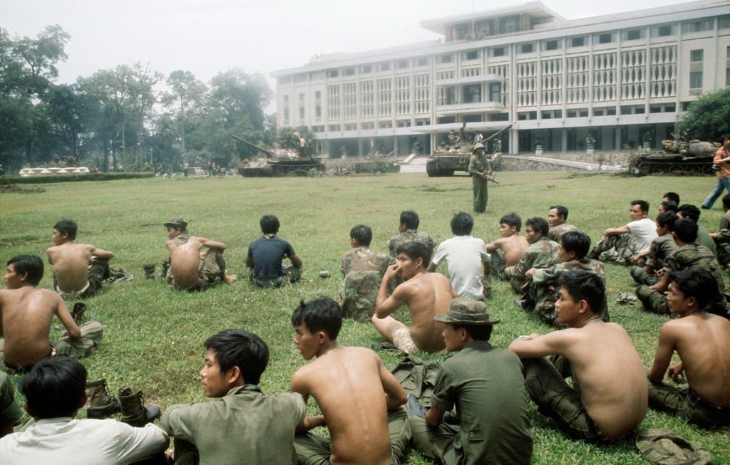 Captured South Vietnamese soldiers sit on a broad lawn after North Vietnamese troops seize the presidential palace in Saigon.