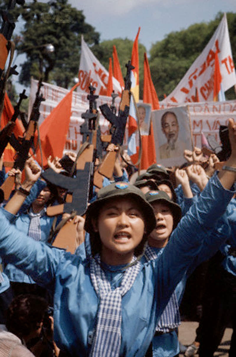 Female North Vietnamese troops enter Saigon carrying wooden rifles, red flags, and portrait of Ho Chi Minh. 30 Apr 1975, Saigon, South Vietnam