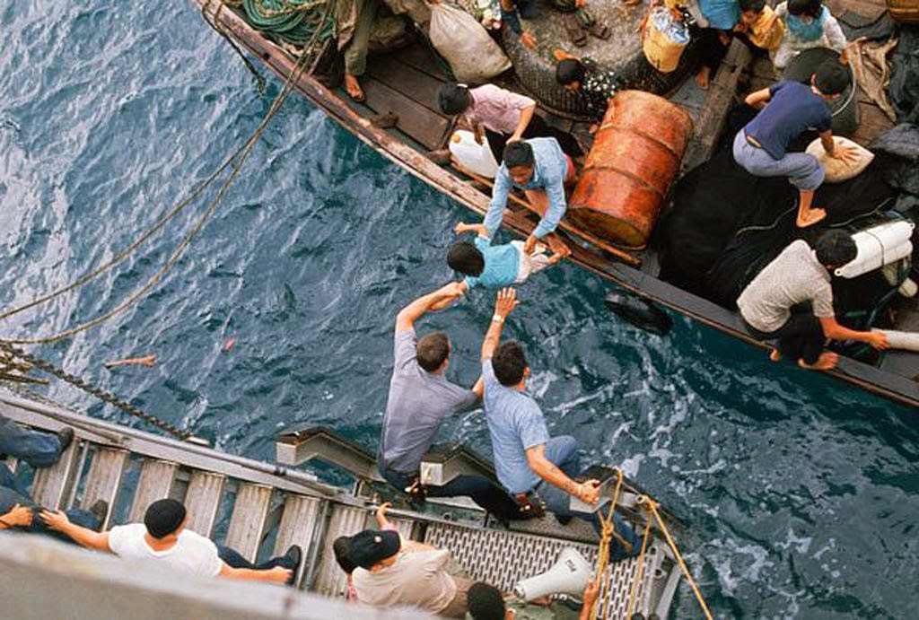 Crewmen of the amphibious cargo ship U.S.S. Durham (LKA-114) take Vietnamese refugees aboard from a small craft.