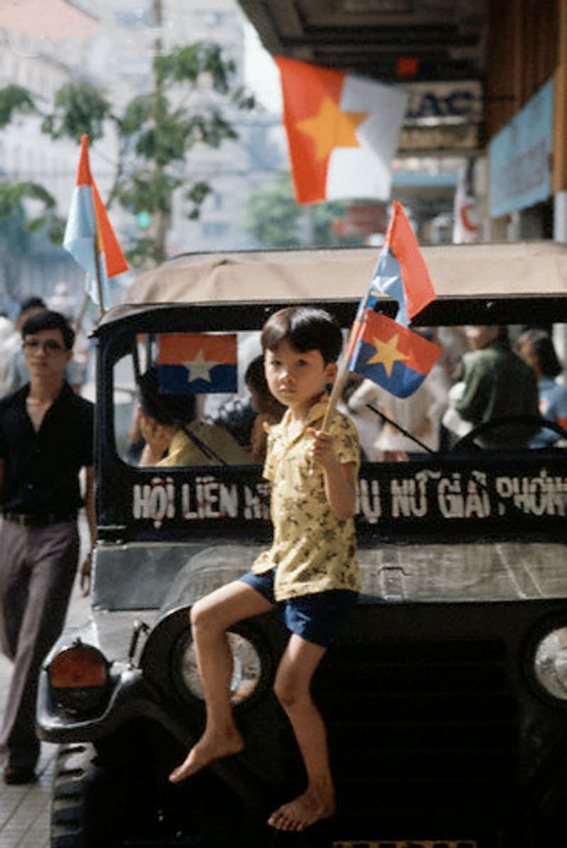 During the Fall of Saigon, a boy on a jeep waves a transitional flag (used for 4 months in the middle of 1975) for South Vietnam, soon to reunite with the North.