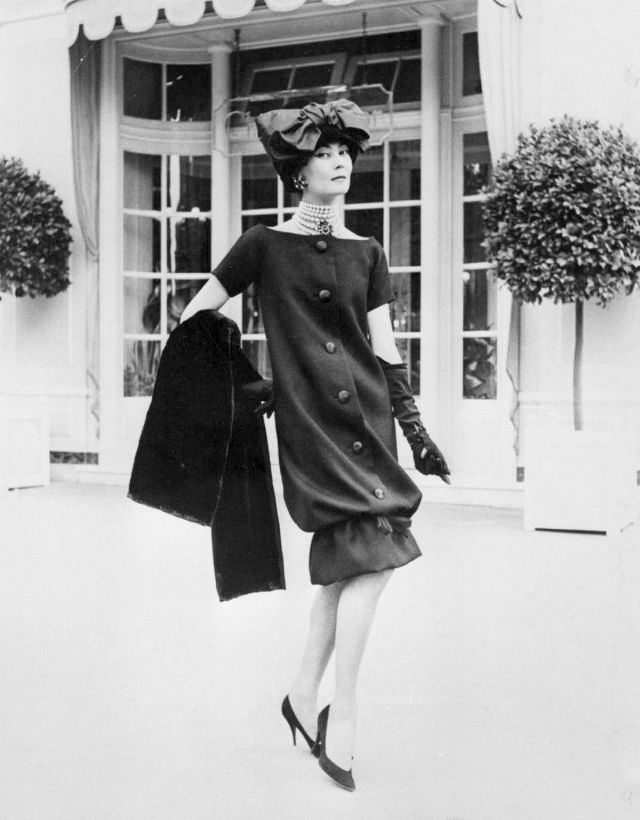Alla outside Maison Dior in Paris, wearing YSL for Christian Dior (of the collection for the Autumn/Winter 1959/60), shoes by Roger Vivier for Christian Dior
