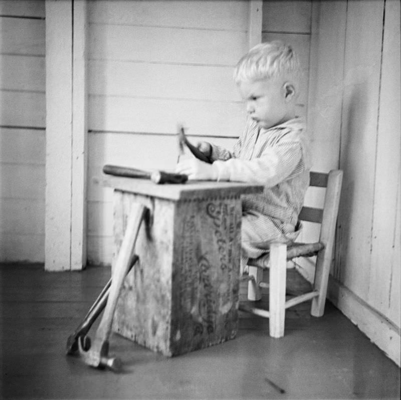 Boy sitting in child-size chair, holding a tool at a workbench
