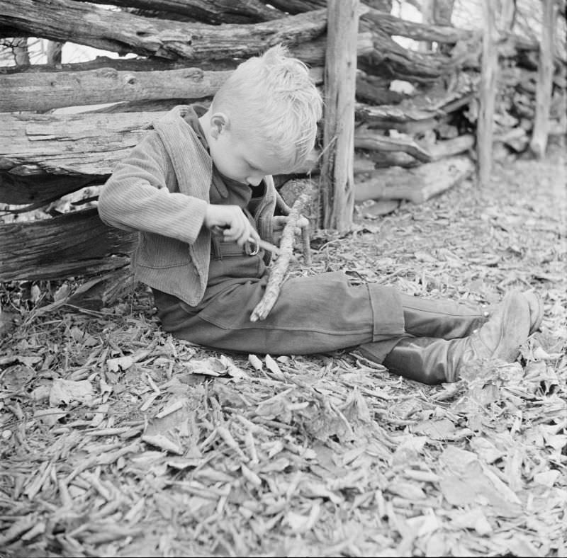 Boy sitting on ground outside, holding two sticks