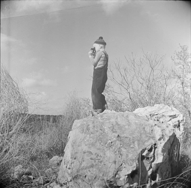 Boy standing on top of a large rock, holding a camera up to his face