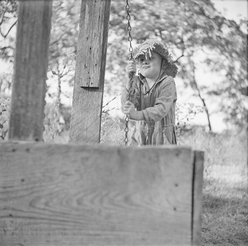 Boy wearing a straw hat, pulling on a metal line, presumably part of a well