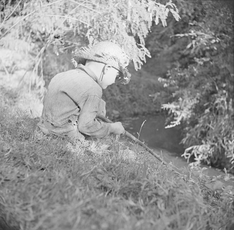 Boy wearing a straw hat, sitting outside with a stick