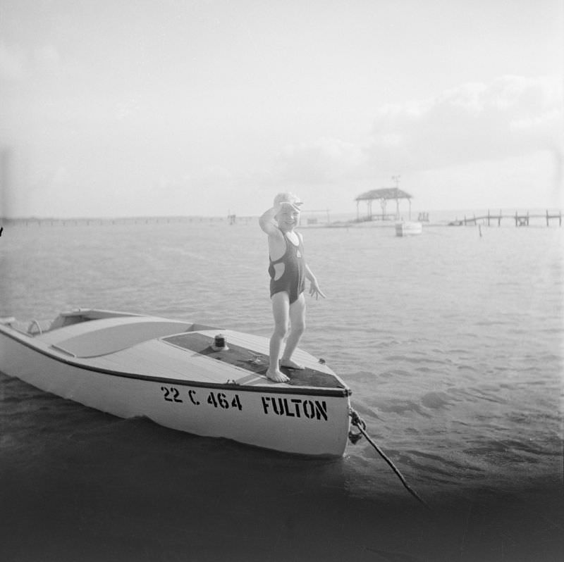 Boy wearing a swim suit, standing on top of a boat named 22 C 464 Fulton