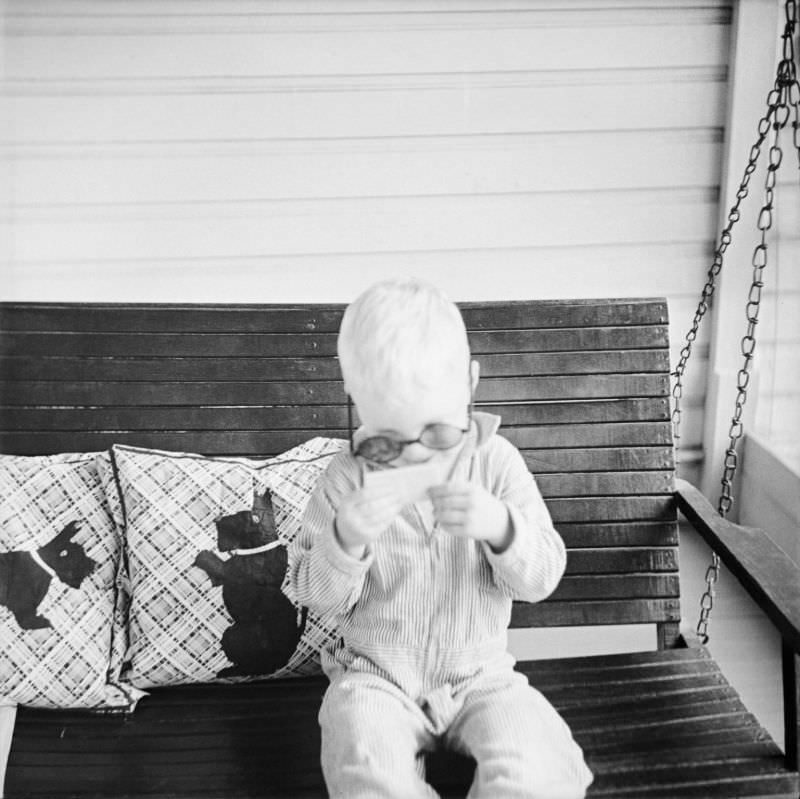 Boy wearing sunglasses, sitting on porch swing